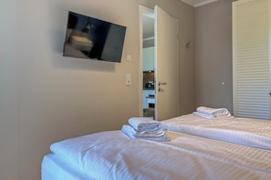 Ein Hotelzimmer mit zwei Betten, einem an der Wand befestigten Fernseher und einer Tür zum Badezimmer.