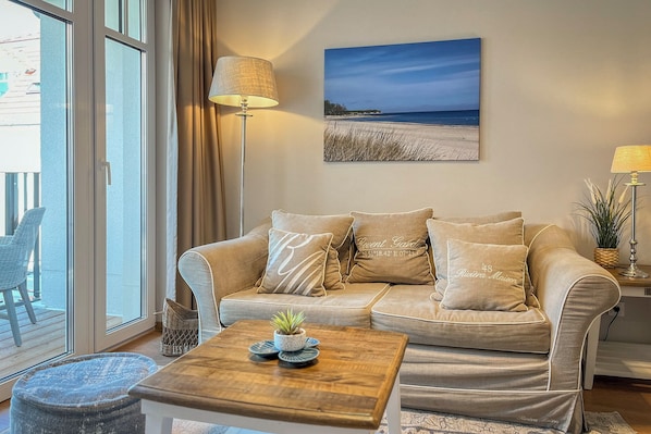 Ein Wohnzimmer mit beiger Couch, Couchtisch aus Holz und einem Gemälde mit Meerblick.