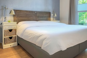 Ein ordentlich bezogenes Bett mit weißen Leinentüchern, ein Holz-Kopfteil, Nachttische mit Lampen und Korbwäschekörbe.
