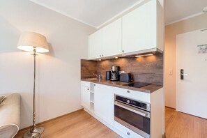 A compact kitchenette with a built-in oven, a coffee maker, and a sink. - Baltischer Hof 26 Apartment (Ostseebad Boltenhagen)