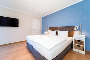 A bedroom with a large bed, bedside lamps, a flat-screen TV, and a nightstand with baskets. - Baltischer Hof apartment 38 (Ostseebad Boltenhagen)