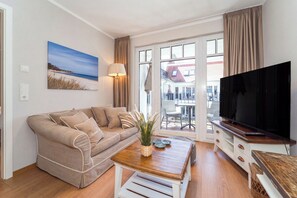 A living room with a sofa, a coffee table, a TV, and a balcony with a view. - Baltischer Hof apartment 38 (Ostseebad Boltenhagen)