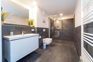 A modern bathroom with a large mirror, a white vanity, a toilet, and a glass-enclosed shower area. - Baltischer Hof apartment 38 (Ostseebad Boltenhagen)
