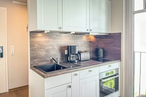 Eine moderne Küche mit weißen Schränken, einer Holzausziehtafel, einem eingebauten Backofen und einer Kaffeemaschine.