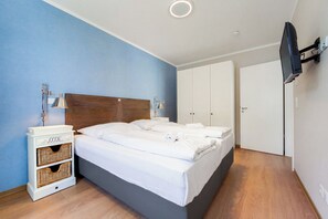 Un dormitorio con cama, lámparas de noche, televisor montado en la pared y armario.