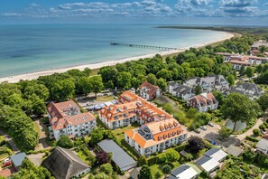 Eine Vogelperspektive zeigt eine Küstenwohngegend mit Strand, einem Steg und Häusern mit roten Ziegeldächern.