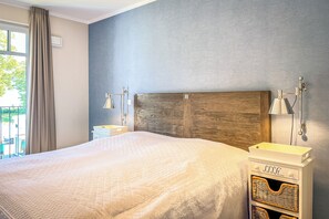 Ein Schlafzimmer mit einem großen Bett, Nachttischen mit Lampen, einem Holz-Kopfteil und Blick ins Freie.