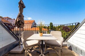 Ein Balkon mit Tisch und Stühlen, einem Blumentopf und Blick auf Gebäude und Grünflächen.