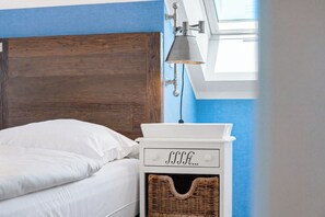 A bed with white bedding, a wooden headboard, a white nightstand with a lamp, and a wicker basket. - Baltischer Hof apartment 67 (Ostseebad Boltenhagen)