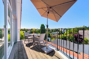 Ein Balkon mit Tisch und Stühlen, einem großen Sonnenschirm und Blick auf eine Wohngegend.