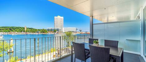 A balcony with a table and chairs overlooking a waterfront with boats and buildings.
