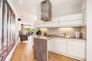 A modern kitchen with white cabinets, a marble countertop, and a stainless steel range hood. - Promenade Villa 03, Apartment 06 (Lübeck-Travemünde)