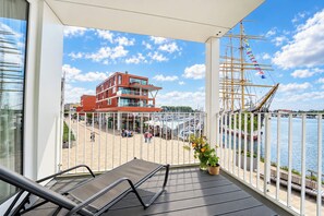 A balcony with a view of a marina, a red building, and a sailboat. - Promenade Villa 03, Apartment 04 (Lübeck-Travemünde)