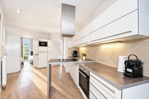 A modern kitchen with white cabinetry, a stainless steel range hood, and a coffee machine. - Promenade Villa 03, Apartment 04 (Lübeck-Travemünde)