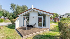 Une petite maison de plain-pied avec une terrasse en bois, une table à manger avec des chaises et une grande porte-fenêtre coulissante.
