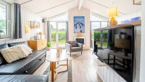 A modern living room with a sofa, a dining table, a TV, and a fireplace. - Vacation home Freibeuterweg 13 (Lübeck-Travemünde)