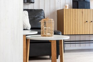 A modern living room with a round white table, a black leather sofa, and a wooden cabinet. - Vacation home Freibeuterweg 13 (Lübeck-Travemünde)