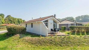 Une maison mobile de plain-pied, dotée d’un toit en pente, d’un petit porche avec une table et des chaises, et d’une antenne parabolique.