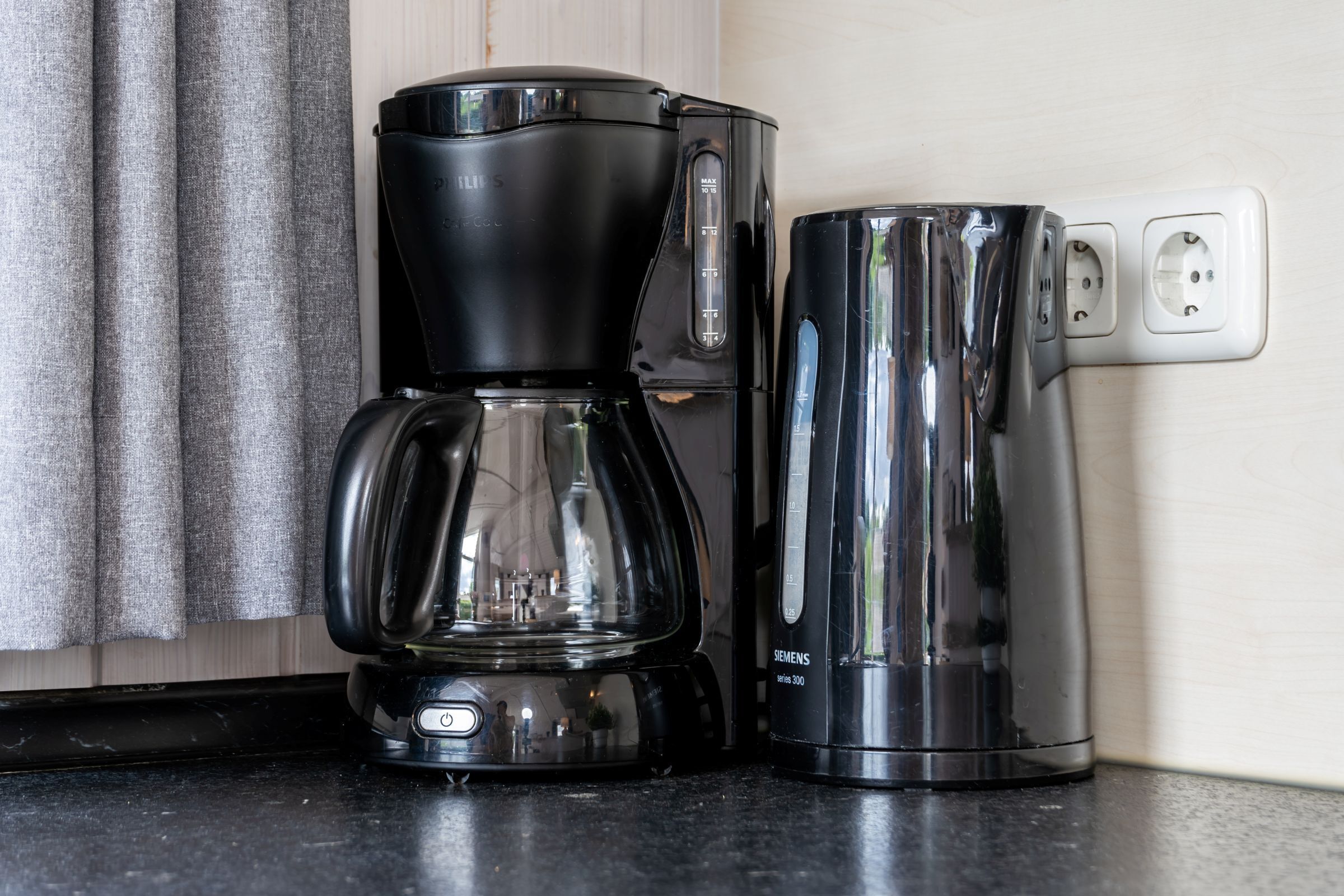 Eine Kaffeemaschine und ein Wasserkocher, beide schwarz, stehen auf einer Küchenarbeitsplatte.