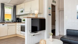 A modern kitchen with a flat-screen TV, wooden cabinets, and a dining area with a black leather couch. - Vacation home Freibeuterweg 13 (Lübeck-Travemünde)