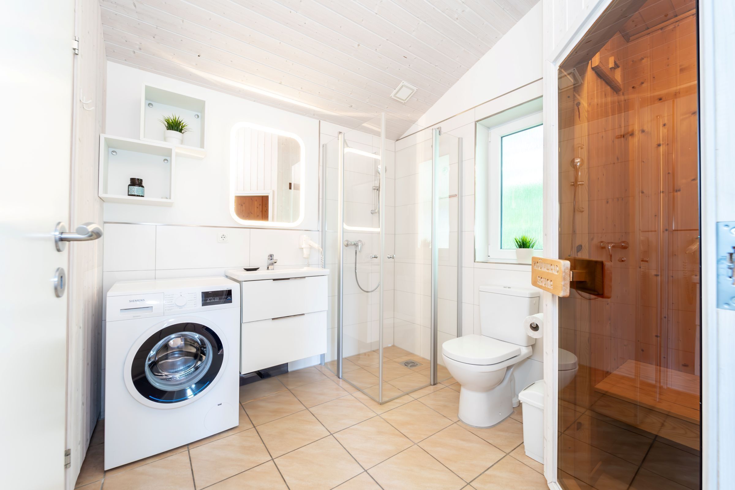 Ein modernes Badezimmer mit Waschmaschine, Toilette und Duschkabine aus Glas.