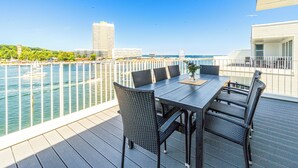 A deck with a table and chairs overlooking a waterfront with buildings and a Ferris wheel in the background. - Promenade Villa 03 Apartment 11 (Lübeck-Travemünde)