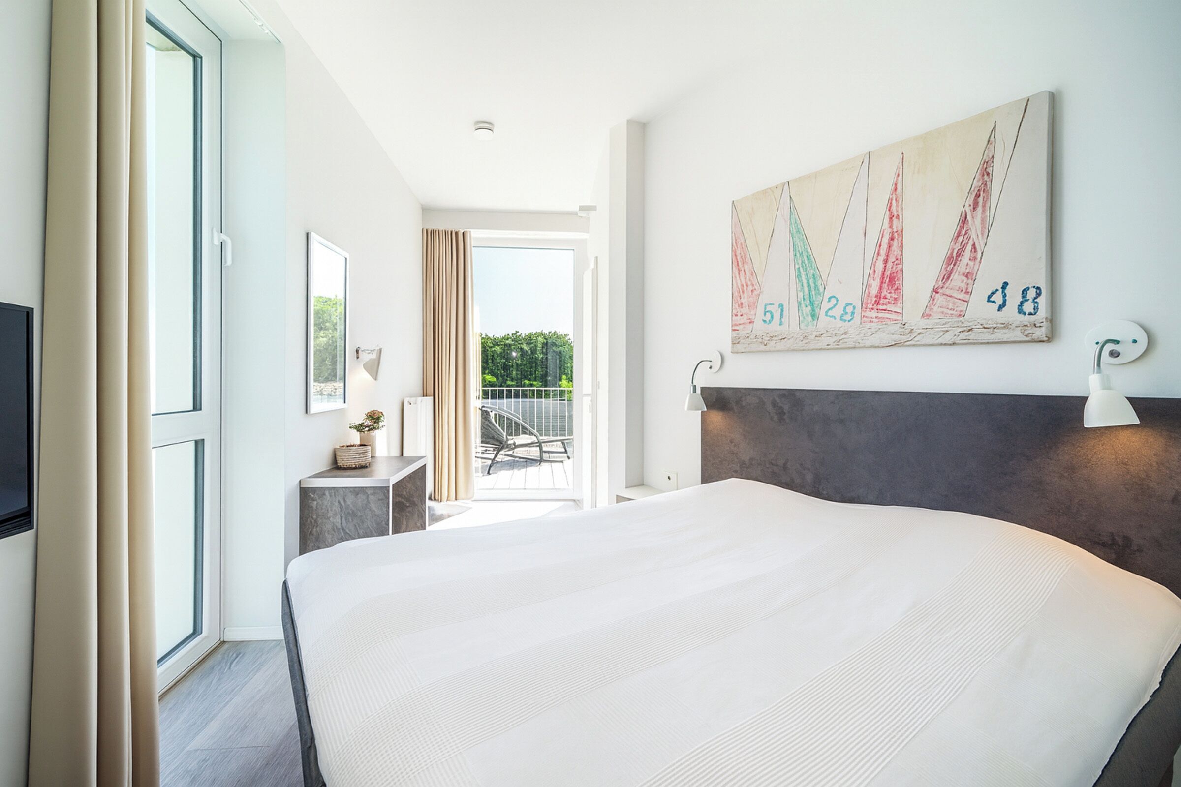Une chambre d’hôtel moderne avec un grand lit, un balcon offrant une belle vue et un tableau représentant un voilier accroché au mur.