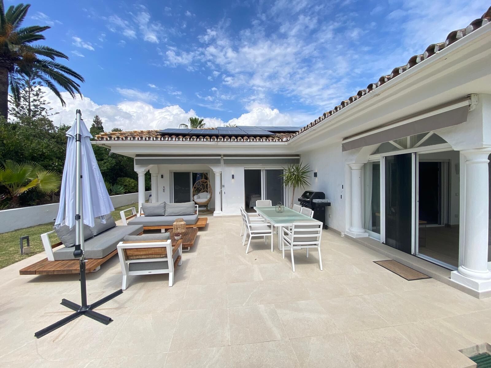 En overdækket terrasse med udendørs møbler, grill og en pergola med parasol.