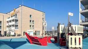 A playground with a red ship play structure, a building with a 'Slow Down' sign, and a clear blue sky. - Vacation home Schatzkiste 18 (Lübeck-Travemünde)