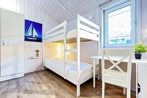 Een kamer met een stapelbed, een bureau en een stoel. Er is een raam met uitzicht op een gebouw en een schilderij van een zeilboot aan de muur.
