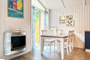 Een eetruimte met een houten tafel en stoelen, een open haard en een groot raam met gordijnen.