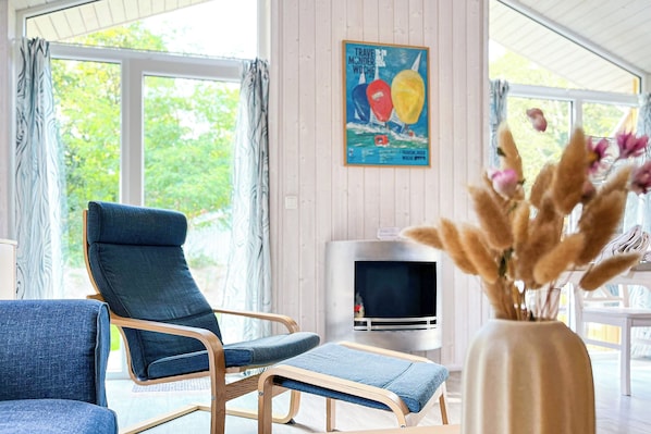 Een moderne woonkamer met een blauwe bank, een fauteuil met houten armleuningen en een televisie.
