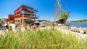 Ein Gebäude am Wasser mit mehreren Stockwerken, eine Anlegestelle mit einem hohen Schiff und einem Fußgängerweg.