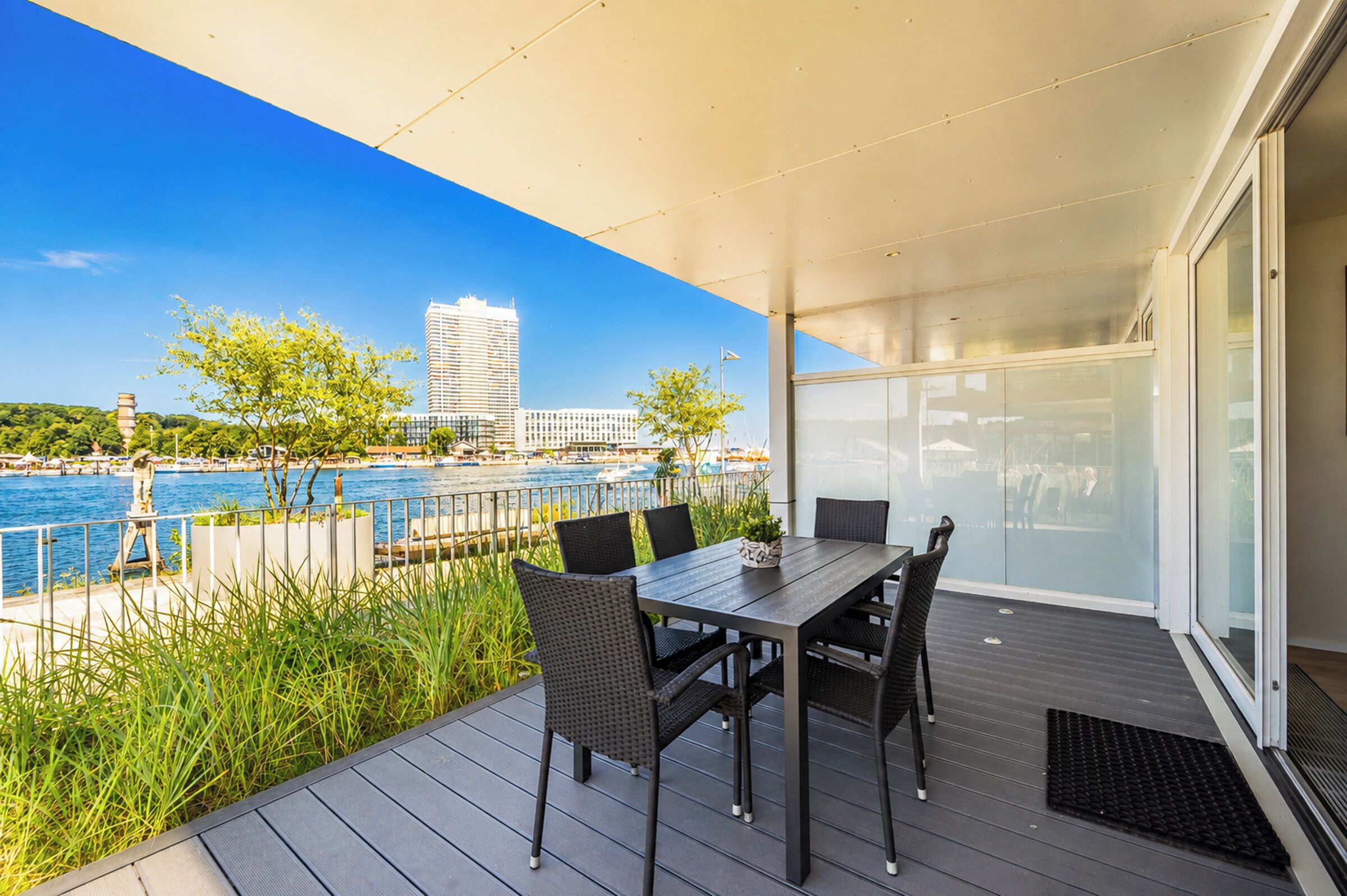 A deck with a table and chairs overlooking a body of water with boats and buildings in the background.