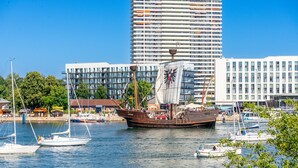 Un gran barco velero amarrado en un puerto deportivo, con edificios modernos al fondo.