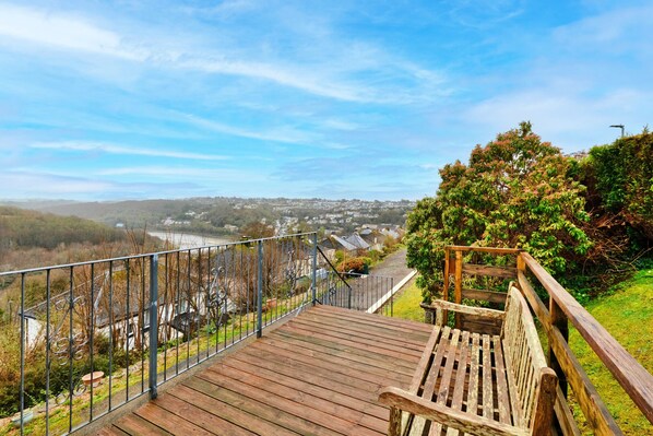 A wooden deck with a metal railing overlooking a residential area and a river.