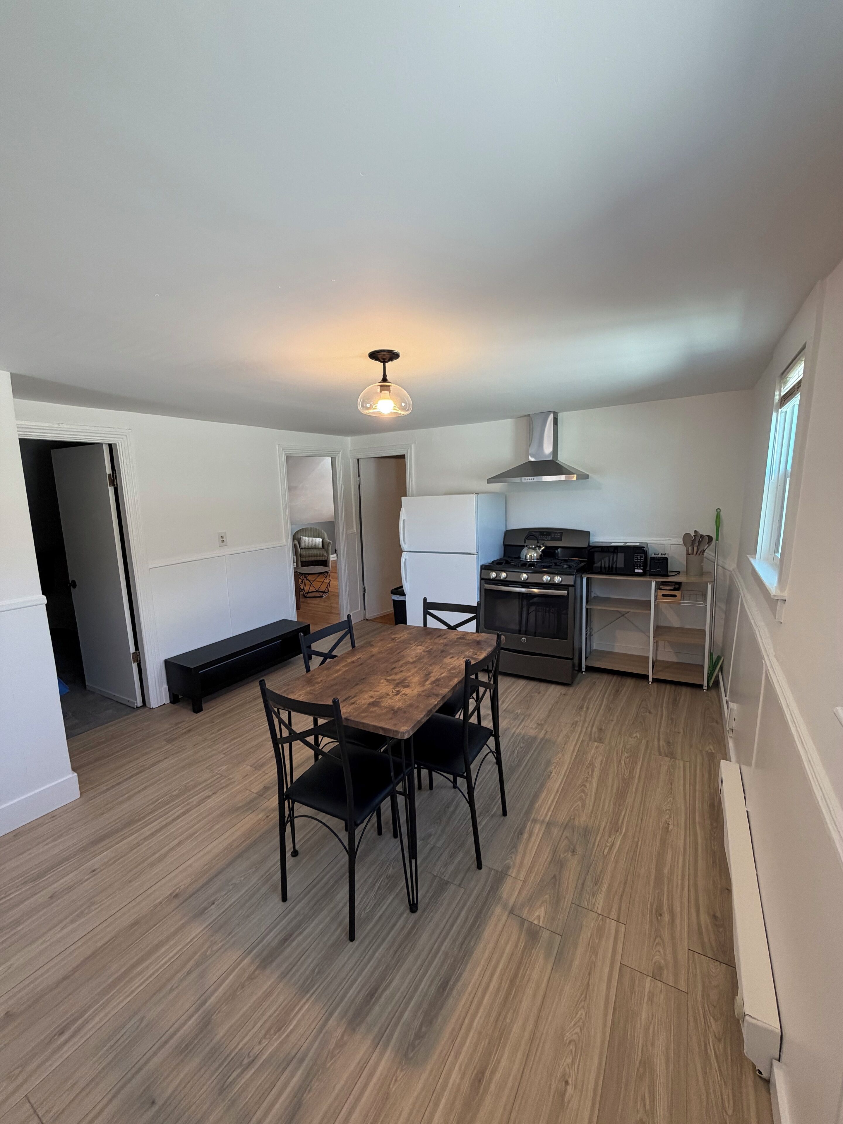 A compact kitchen with a dining area, wooden flooring, and a hanging light fixture.