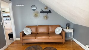 Un saló modern amb un sofà de cuir marró, dos tamborets hexagonals, una taula auxiliar blanca i decoració mural.