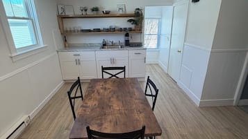Zona pranzo con tavolo e sedie in legno, cucina con mobili bianchi e lampadario.
