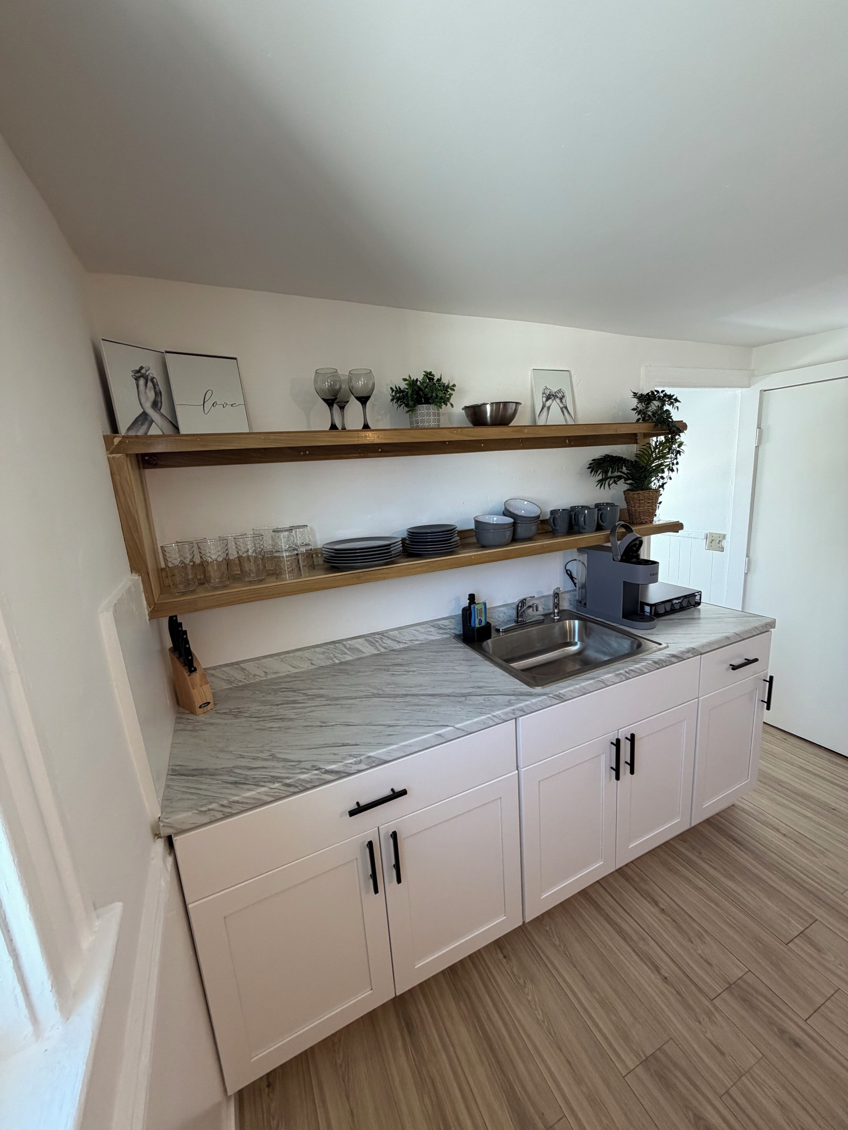 Cocina con encimeras de mármol, armarios blancos y estantes de madera.