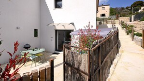 Ein weißes Gebäude mit einer Terrasse, einem überdachten Sitzbereich und einem Holzzaun.