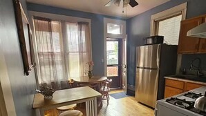 Una cocina compacta con piso de madera, un refrigerador, estufa y ventilador de techo.