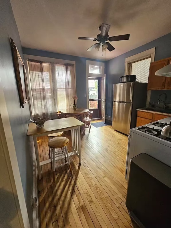 Una cocina compacta con piso de madera, un refrigerador, estufa y ventilador de techo.
