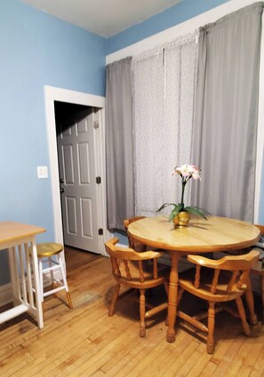 Un comedor con una mesa redonda de madera y sillas, un jarrón con flores y un radiador blanco.