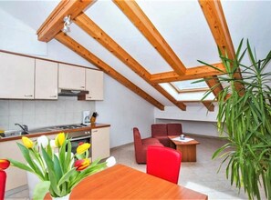 A modern kitchen with wooden beams, a dining area with red chairs, and a large skylight. - Apartments Macolić Rab (Rab)