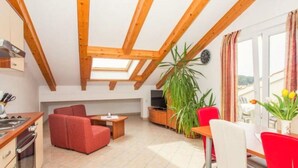 A cozy apartment with a kitchen, dining area, and living room. It features wooden beams, a skylight, and a large window with curtains. - Apartments Macolić Rab (Rab)