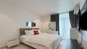 A modern hotel room with a large bed, a bedside table, a dresser, a mirror, and a flat-screen TV. - Opulent 1 Bedroom suite in Embassy Gardens (Accra)