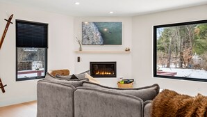 Una sala de estar moderna con chimenea, un televisor grande y vistas a un paisaje nevado.