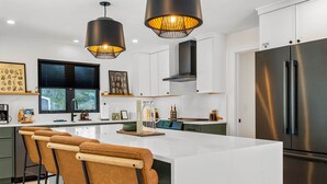 Una cocina moderna con una isla grande, electrodomésticos de acero inoxidable, iluminación colgante y taburetes de bar.