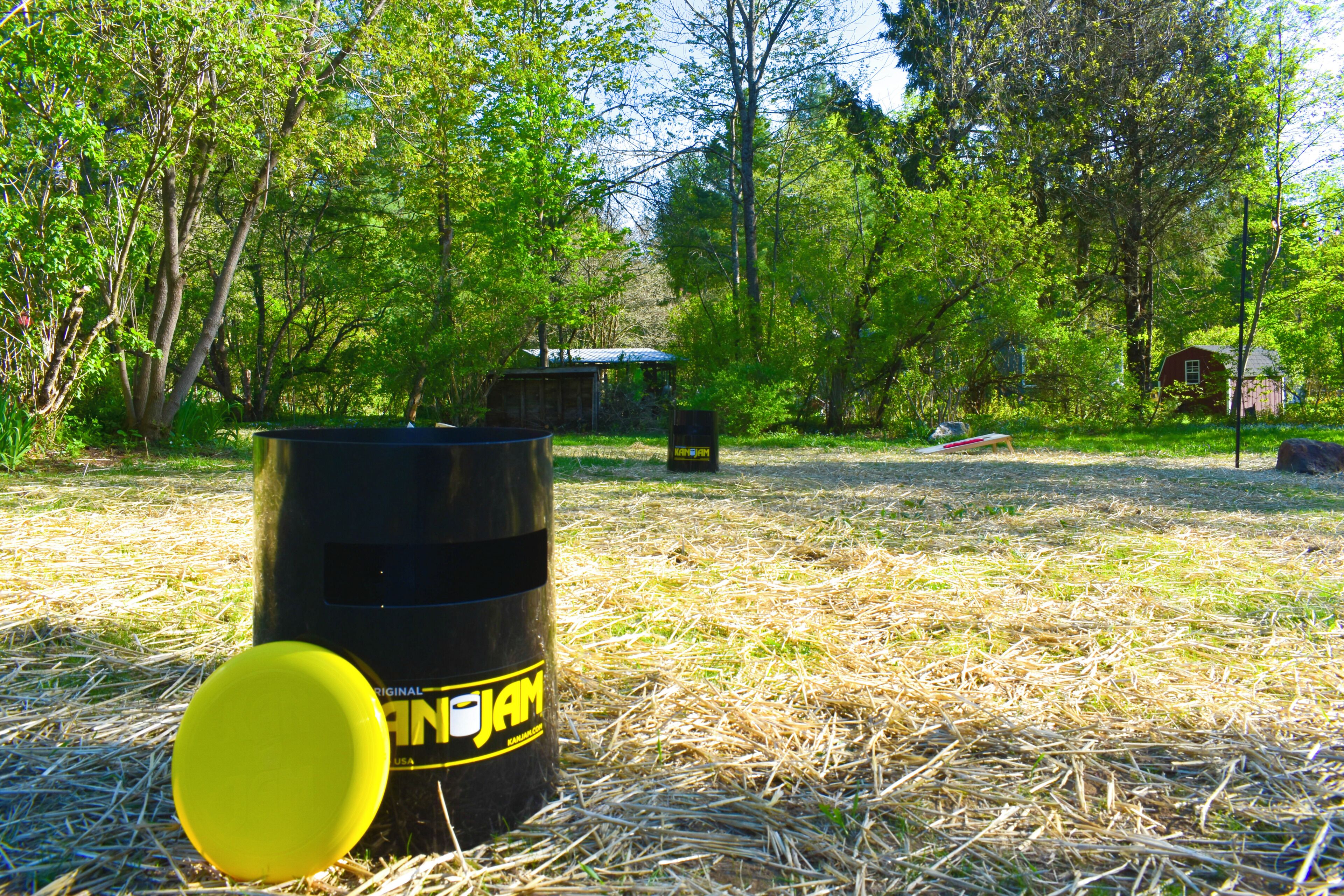 Un décor extérieur en milieu rural, avec un baril noir portant l’inscription « JAM » et un objet jaune posé sur le sol.